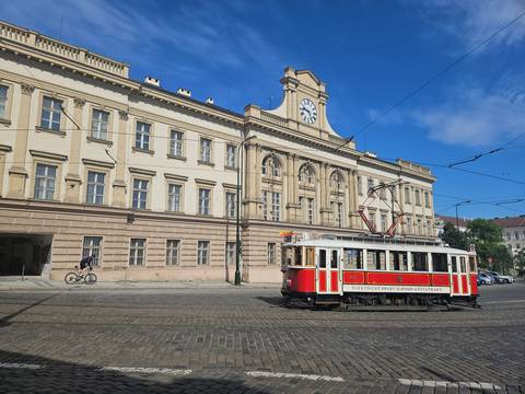 Vintage red tram passing a historic cream-coloured building with clock tower.