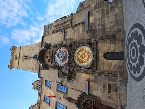 Tall Prague Astronomical Clock tower with ornate dial viewed from street level.