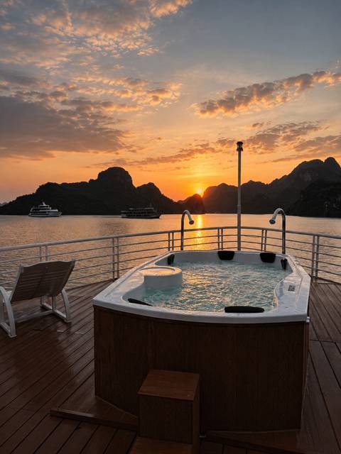 Hot tub on a cruise deck facing dramatic karst islands as the sun sets over Halong Bay.
