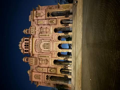 Night view of the illuminated pink Patrika Gate palace facade with deep blue sky above.