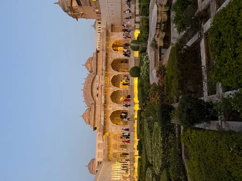 Illuminated Mughal garden courtyard at dusk with visitors strolling past elegant sandstone arches.