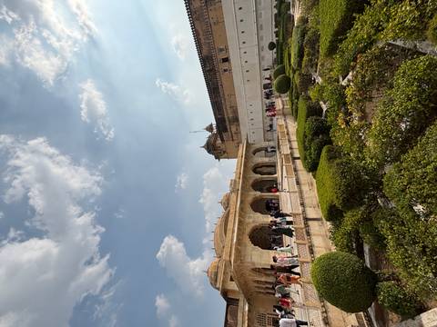 Visitors wander through the ornate sandstone arches and manicured garden courtyards of Amber Fort under a bright sky.