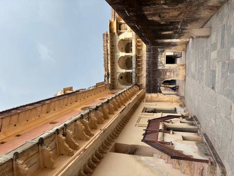 Stone corridors, balconies, and arches of an inner courtyard at Amber Fort with a lone visitor in the distance.