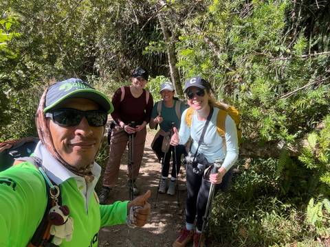 Trekking guide and hikers with poles smile on a lush forest trail.