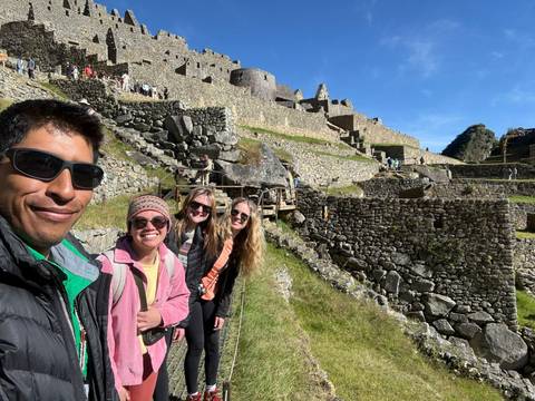 Smiling trekkers stand on stone terraces of Machu Picchu with ruins rising behind them.