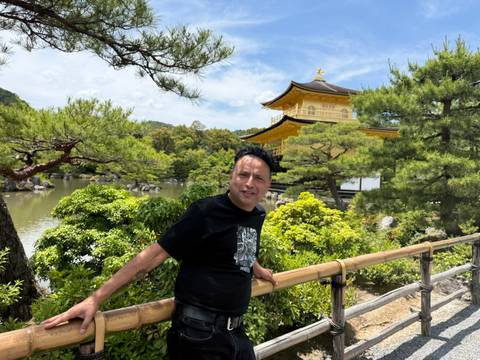 Traveler poses on a wooden bridge with the Golden Pavilion temple and pond garden behind