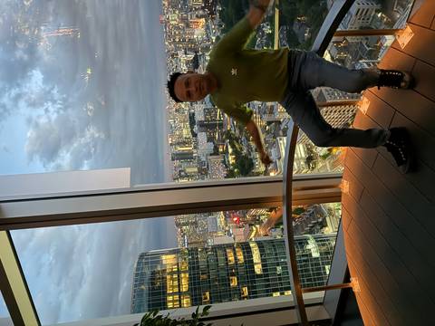 Man poses inside a high-rise observation deck overlooking Tokyo city lights at dusk