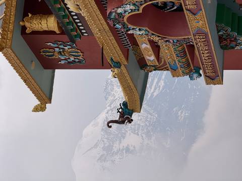 Ornate Tibetan-style monastery eaves decorated with vibrant carvings, backed by a snowy peak.
