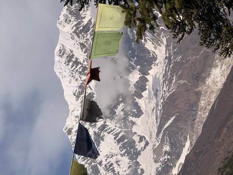 Prayer flags flutter in the foreground framing a dramatic ice-covered Himalayan face.