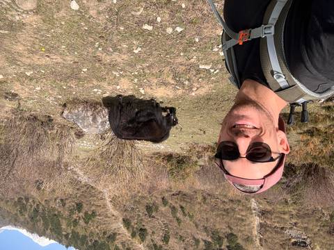 Smiling trekker selfies with a grazing yak on an alpine meadow trail.