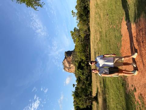 Couple pose in an open field with the massive rock fortress of Sigiriya rising behind.