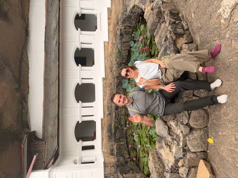 Travellers seated barefoot beside a lotus pond at a white temple built into rock.