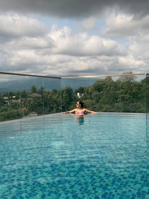 Woman relaxes in an infinity pool with jungle hills and mountains in the distance.