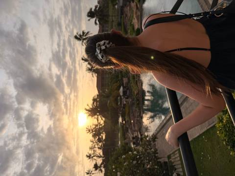 Back view of woman watching tropical sunset over resort pool and palms.