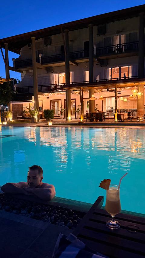 Evening view across a lit swimming pool to a stylish open-air resort restaurant.