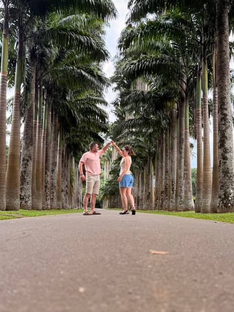 Couple dances in a grand avenue of tall royal palms in a botanical garden.