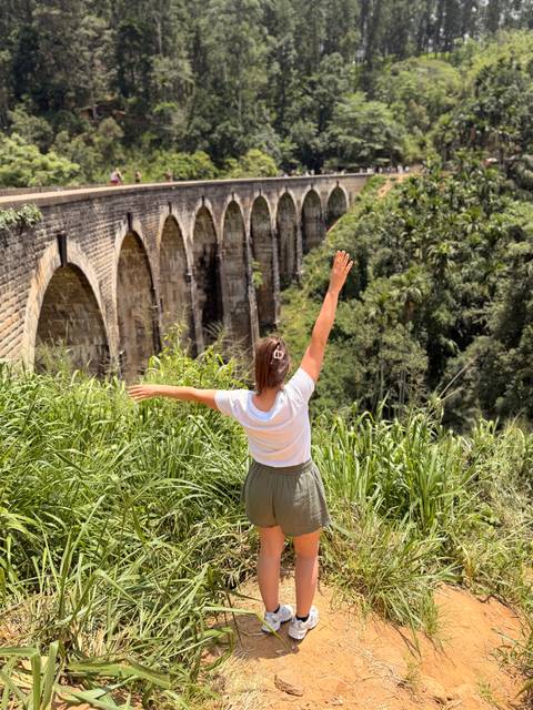 Traveller stretches arms toward the famous Nine-Arch Bridge amid lush jungle.