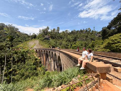 Couple sits on the parapet of Nine-Arch Bridge enjoying panoramic jungle views beside the railway.