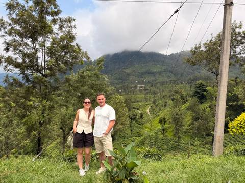 Couple poses in misty tea country with green hills rising into low clouds.