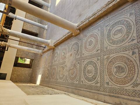 Long corridor of intricate Roman floor mosaics framed by marble columns.
