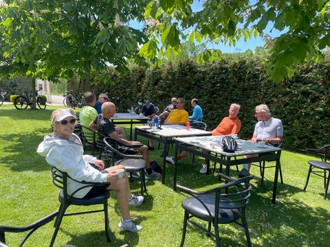 Cyclists rest at shaded garden tables enjoying drinks after a ride.