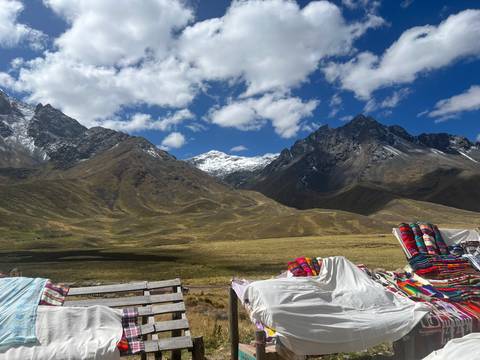 Snow-capped peaks and rugged valley under blue sky with colorful Andean blankets displayed in the foreground