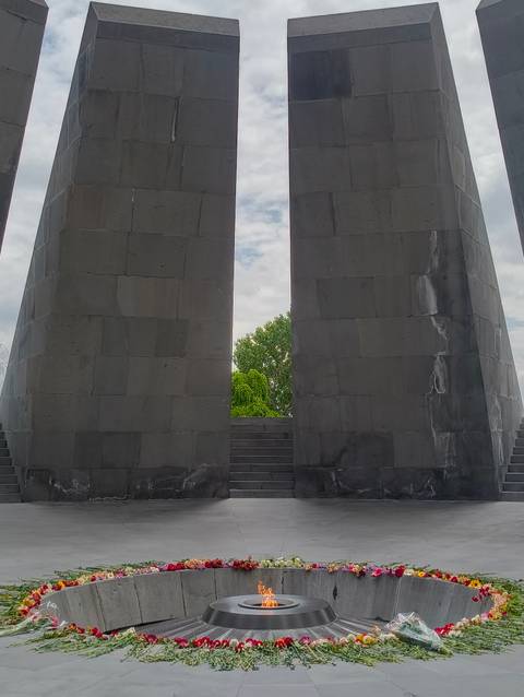 Two massive basalt pillars with a narrow gap framing green trees and cloudy sky, part of a solemn memorial complex.