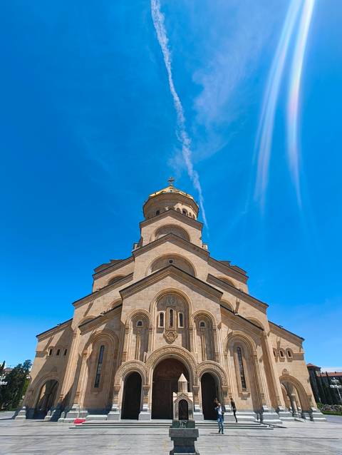Low-angle shot of the Holy Trinity Cathedral’s golden dome and arched stone tiers contrasted against a vivid blue sky.