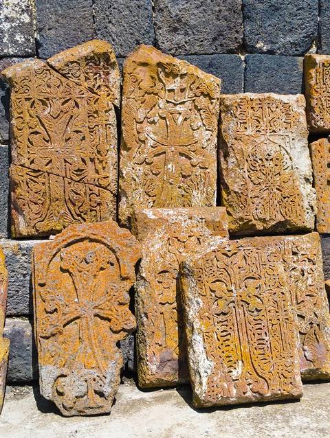 Close-up of intricately carved rusty-orange Armenian khachkar stone crosses stacked together.