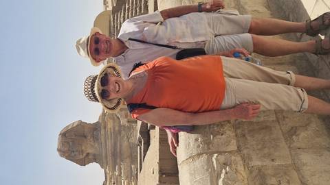 Older couple standing near the Sphinx with bright midday sun overhead on the Giza Plateau.