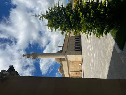 Spacious courtyard of a grand mosque with slender minaret, domes and stone arcade framed by greenery.