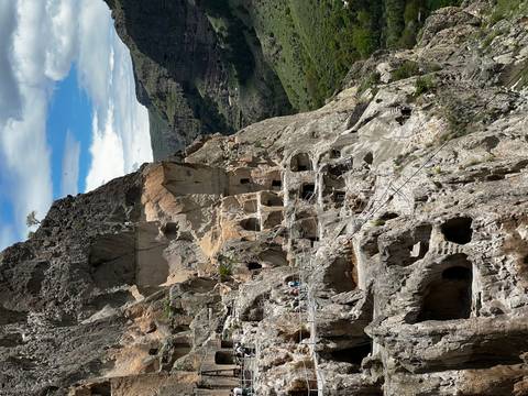 Spectacular cliff-side cave city with multiple rock-cut dwellings and visitors walking along narrow paths above a lush valley.