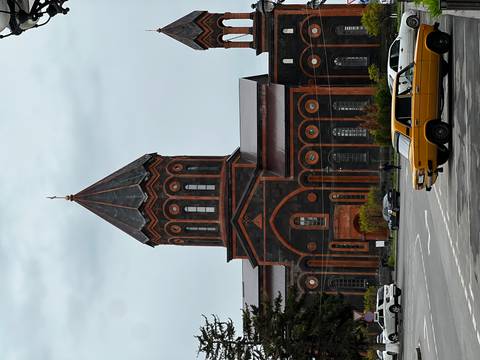 Distinctive black and red tuff stone church with tall conical spire; classic Soviet-era cars parked in front.