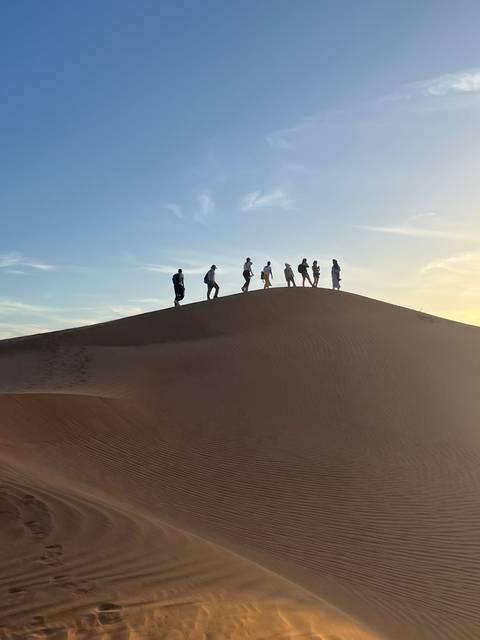 Silhouetted travellers walking along a dune crest at dusk.