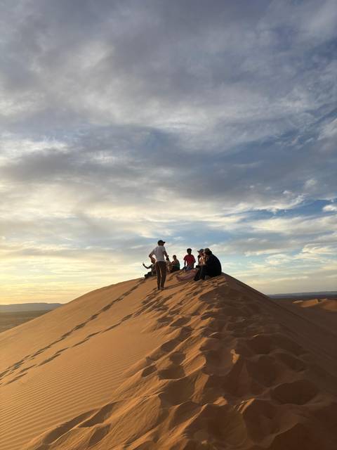 Travellers resting atop a dune under dramatic evening clouds.
