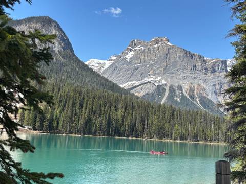 Vivid emerald lake with a red canoe gliding beneath soaring conifer-clad mountains.