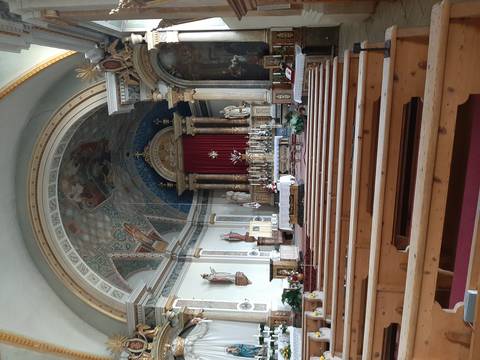 Richly decorated church interior with frescoed dome, gilded altar and wooden pews.