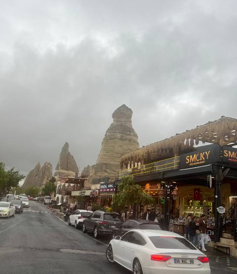 Iconic fairy-chimney rock rises beside lively cafés and shops beneath grey skies in Göreme.