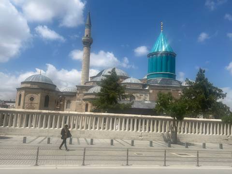 The turquoise-tiled dome and minaret of the Mevlana Museum gleam against a bright sky.