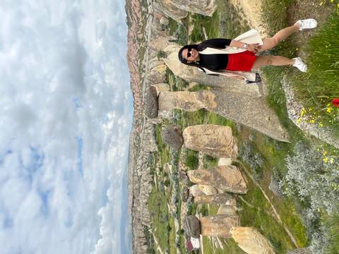 Traveler poses beside surreal balancing rock columns amid lush spring flowers in Cappadocia.