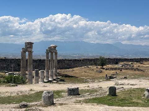 Standing marble columns of ancient Hierapolis overlook a vast plain and hazy mountains.