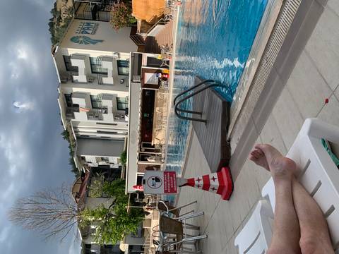 Relaxing poolside scene at a resort with loungers, feet up, and modern apartments behind.