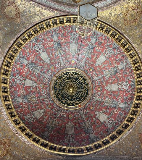 Highly detailed red and gold Ottoman dome ceiling with intricate calligraphy.