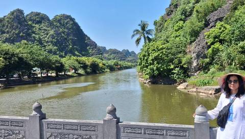 A lush river valley bordered by limestone cliffs and tropical trees, with a lone tourist posing at the balustrade.