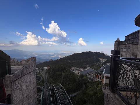 A sweeping mountain panorama from an elevated resort complex with winding alpine slides below and dramatic cloudscape above.