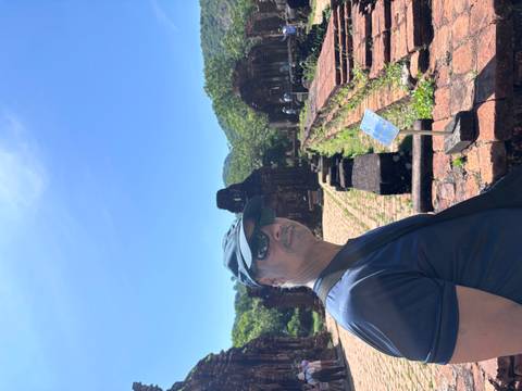 A visitor stands beside ancient brick temple ruins of My Son Sanctuary under a clear blue sky.