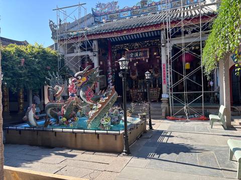 An ornate dragon mosaic fountain stands in a courtyard of a historic Chinese-Vietnamese temple under restoration.