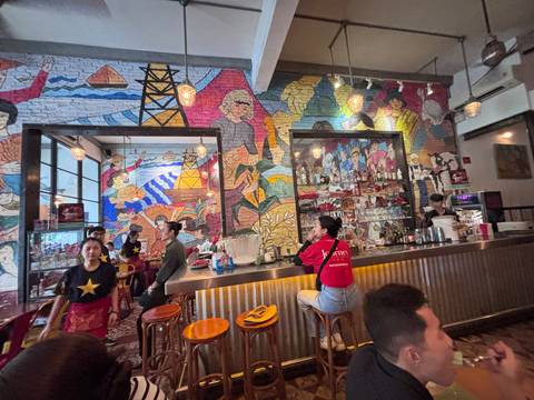 A trendy Vietnamese bar with colourful wall murals, pendant lights and patrons chatting around the counter.