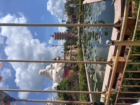 A large seated white Buddha overlooks a lotus pond and pagodas under a dramatic sky.