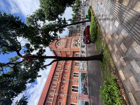 The red-brick façade of Notre-Dame Cathedral Basilica of Saigon partially covered by scaffolding on a rainy day.
